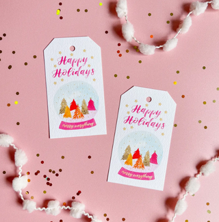 a pair of tags with text and a snow globe on a pink background